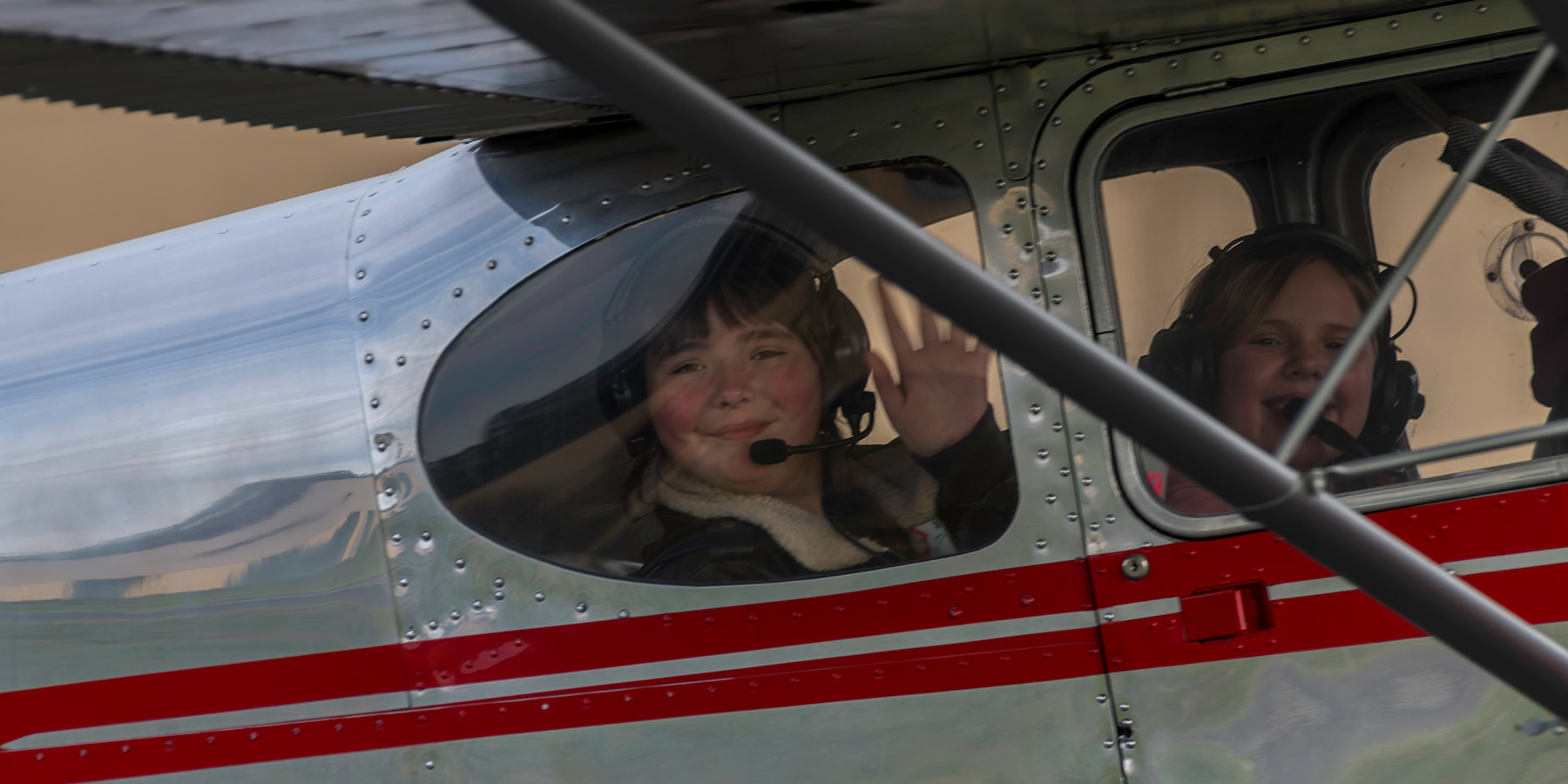 boy waving from the cockpit of a silver and red plane
